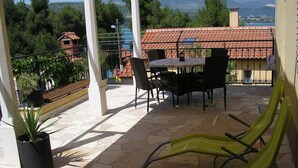 Una terraza con una mesa y sillas, una planta en maceta y vistas a un edificio de tejas rojas y árboles.