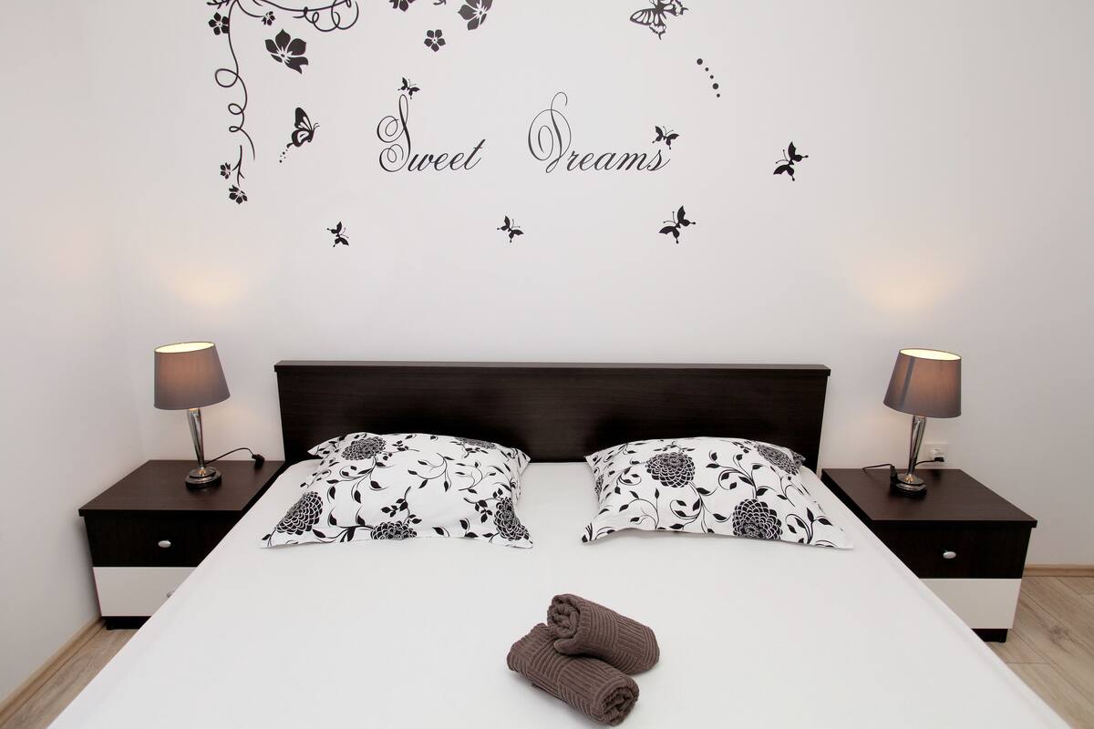 A neatly made bed with floral-patterned pillows, two bedside tables with lamps, and a wall decal with the text "Sweet Dreams".