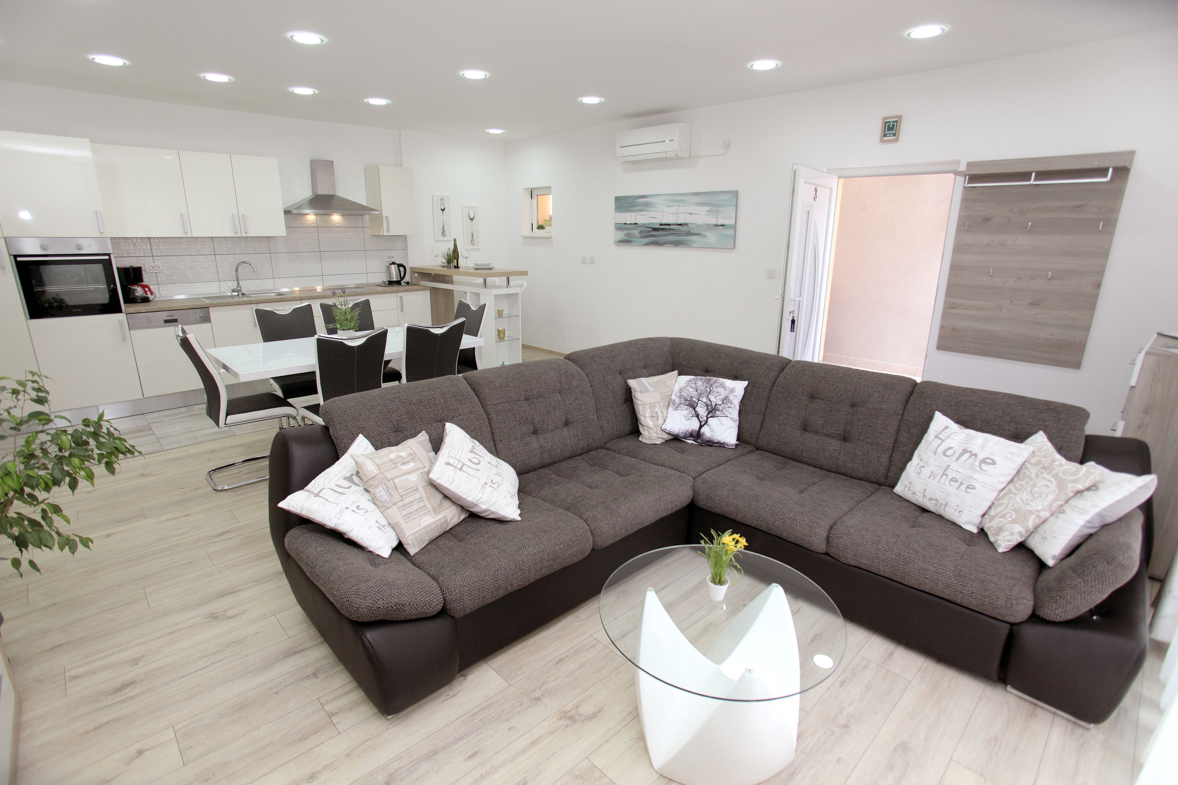 A modern living room with a sectional sofa, a glass coffee table, and a dining area with a white table and chairs.
