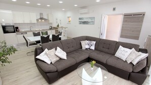 Una sala de estar moderna con un sofá modular, una mesa de centro de vidrio y un comedor con una mesa y sillas blancas.