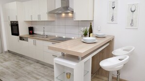 Una cocina moderna con armarios blancos, una campana extractora de acero inoxidable, horno empotrado, encimera de madera y dos taburetes blancos.