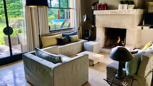 A cozy living room with a fireplace, comfortable seating, and a large window overlooking a garden. - House to rent for 6-12 people in Vaudreuil-27-Louviers-Gaillon- Andé-Rouen (connelles)