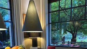 A modern dining area with a long wooden table, white chairs, a bowl of seasonal fruits, and a large window with a view of trees. - House to rent for 6-12 people in Vaudreuil-27-Louviers-Gaillon- Andé-Rouen (connelles)