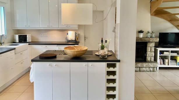 Una cocina moderna con armarios blancos, encimera negra y un refrigerador para vinos empotrado.