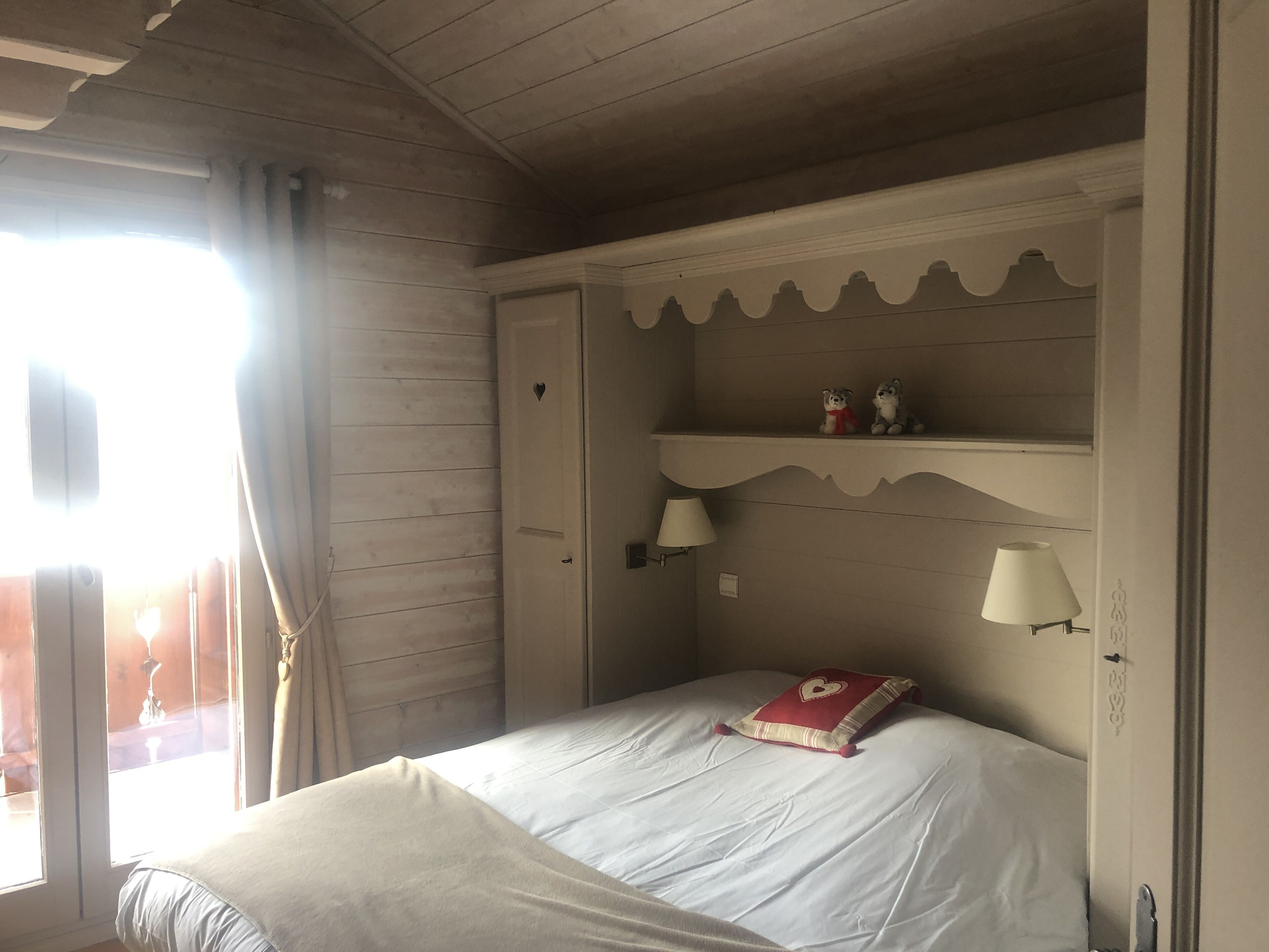 Een slaapkamer met een bed, een nachtkastje, een plank met decoratieve objecten en een raam met gordijnen.