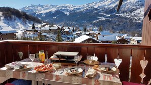 Une table à manger dressée avec de la nourriture et des boissons, donnant sur un village de montagne enneigé.