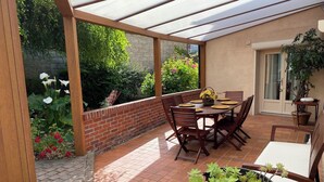 Un patio techado con suelo de ladrillo, una mesa de madera con sillas y una planta en maceta.