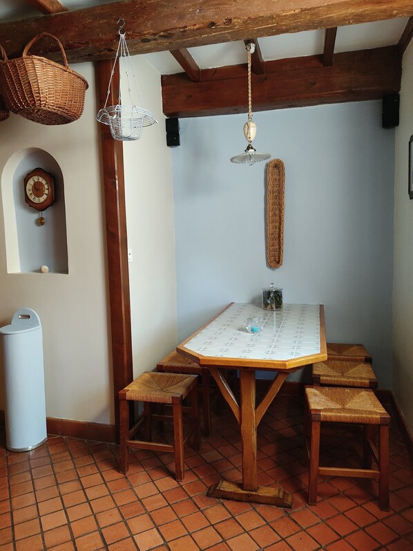 A dining area with a wooden table, benches, a hanging light fixture, a woven basket, and a wall clock. - "LA PERGOLA" COUNTRY HOUSE NEAR ST VALERY SUR SOMME (Lanchères)
