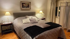 Un dormitorio con una cama grande, dos mesitas de noche con lámparas, un cuadro en la pared y una ventana con cortinas.