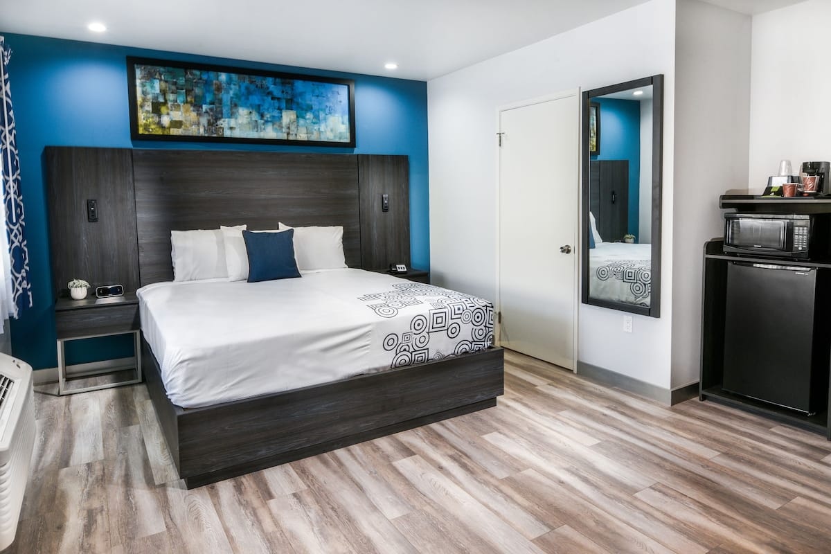 A modern hotel room with a large bed, a small desk, a microwave, and a coffee machine.