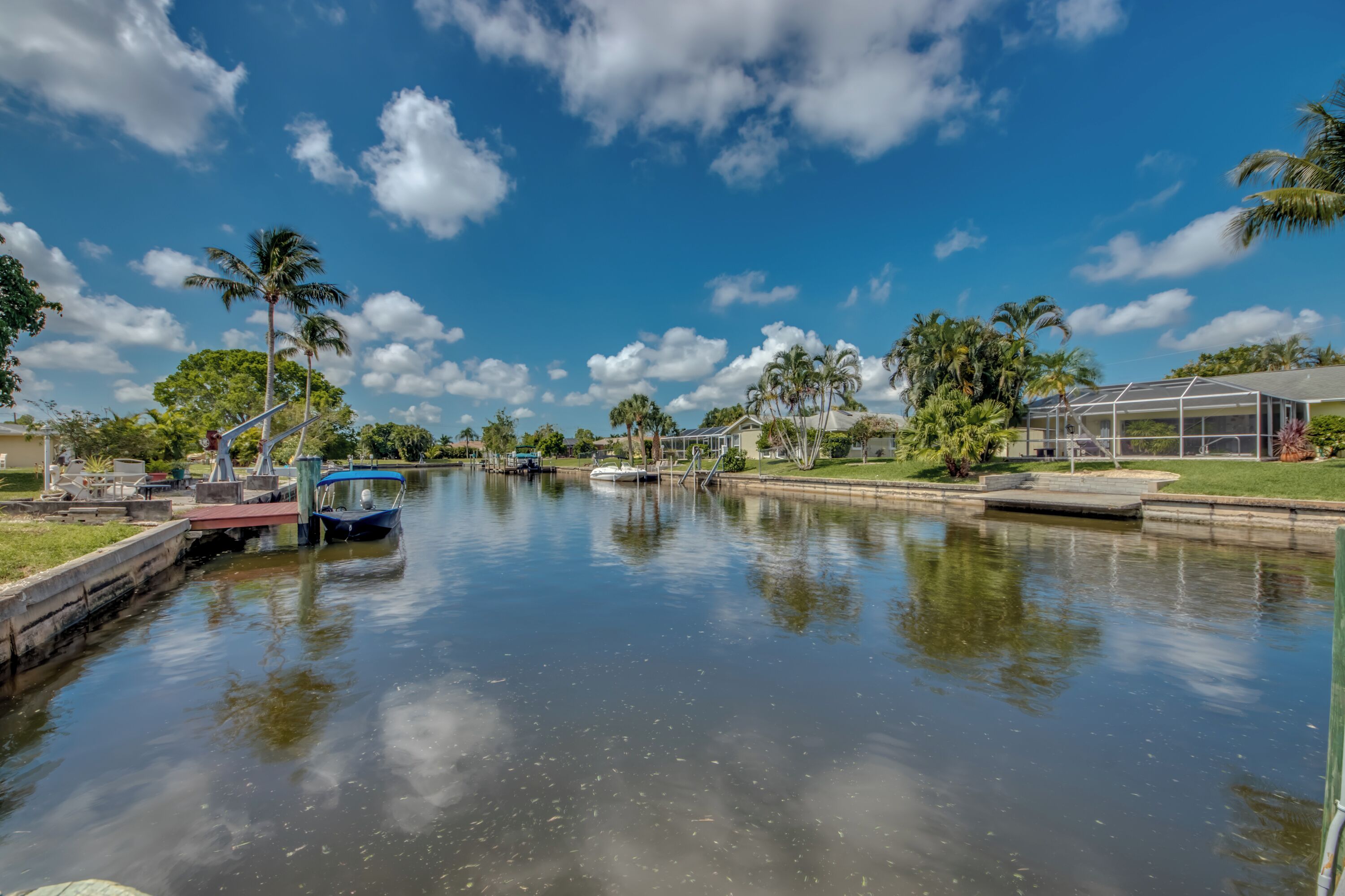 A calm waterway with boats, palm trees, and a house with a covered porch.