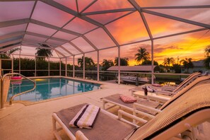 A covered outdoor swimming pool with lounge chairs and a poolside table.