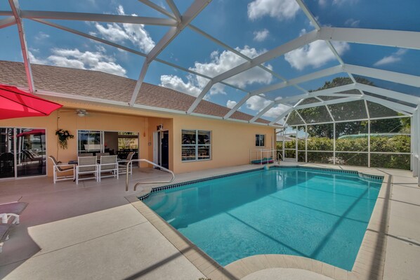 An indoor swimming pool with a glass ceiling, lounge chairs, and a red umbrella.