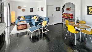Ein modernes Wohnzimmer mit einem blauen Modulsessel, gelben Sesseln, einem Couchtisch und einem Essbereich mit gelben Stühlen und einem runden Tisch.