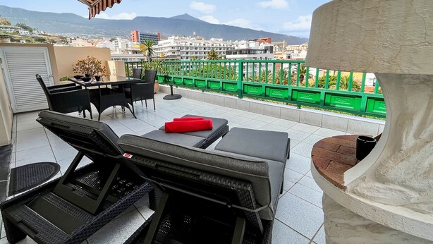 Ein Balkon mit Sitzmöbeln, Blick auf die Stadt und ein Berg im Hintergrund.