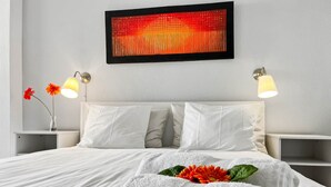 Ein ordentlich bezogenes Bett mit weißen Leinen, zwei Nachttischlampen und einem an der Wand hängenden Kunstwerk.