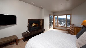 Une chambre avec une cheminée, un grand lit, une télévision et une vue sur un paysage enneigé par une grande fenêtre.