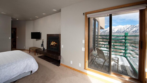Une chambre avec une cheminée, un lit, une télévision et une grande fenêtre donnant sur les montagnes.