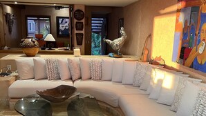 A modern living room with a curved sectional sofa, a glass coffee table, and a ceiling fan. - La Casa Que Ve al Mar te da la bienvenida en 2026! (Zihuatanejo)