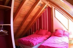 Quarto pequeno com uma cama de solteiro, teto inclinado e vigas de madeira.