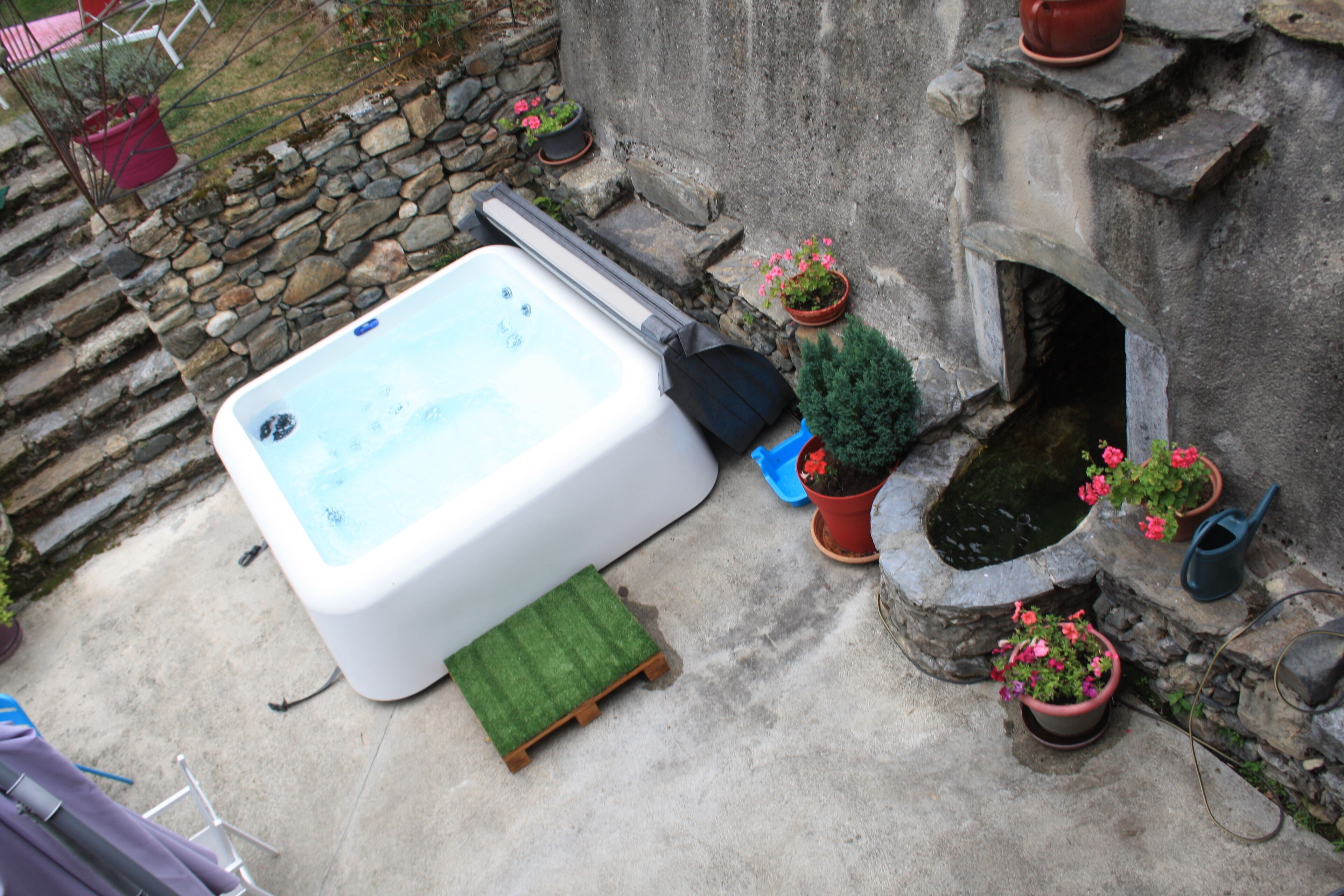 Un bain à remous situé à côté d’un mur de pierres, agrémenté de plantes en pot et d’un petit espace jardin.