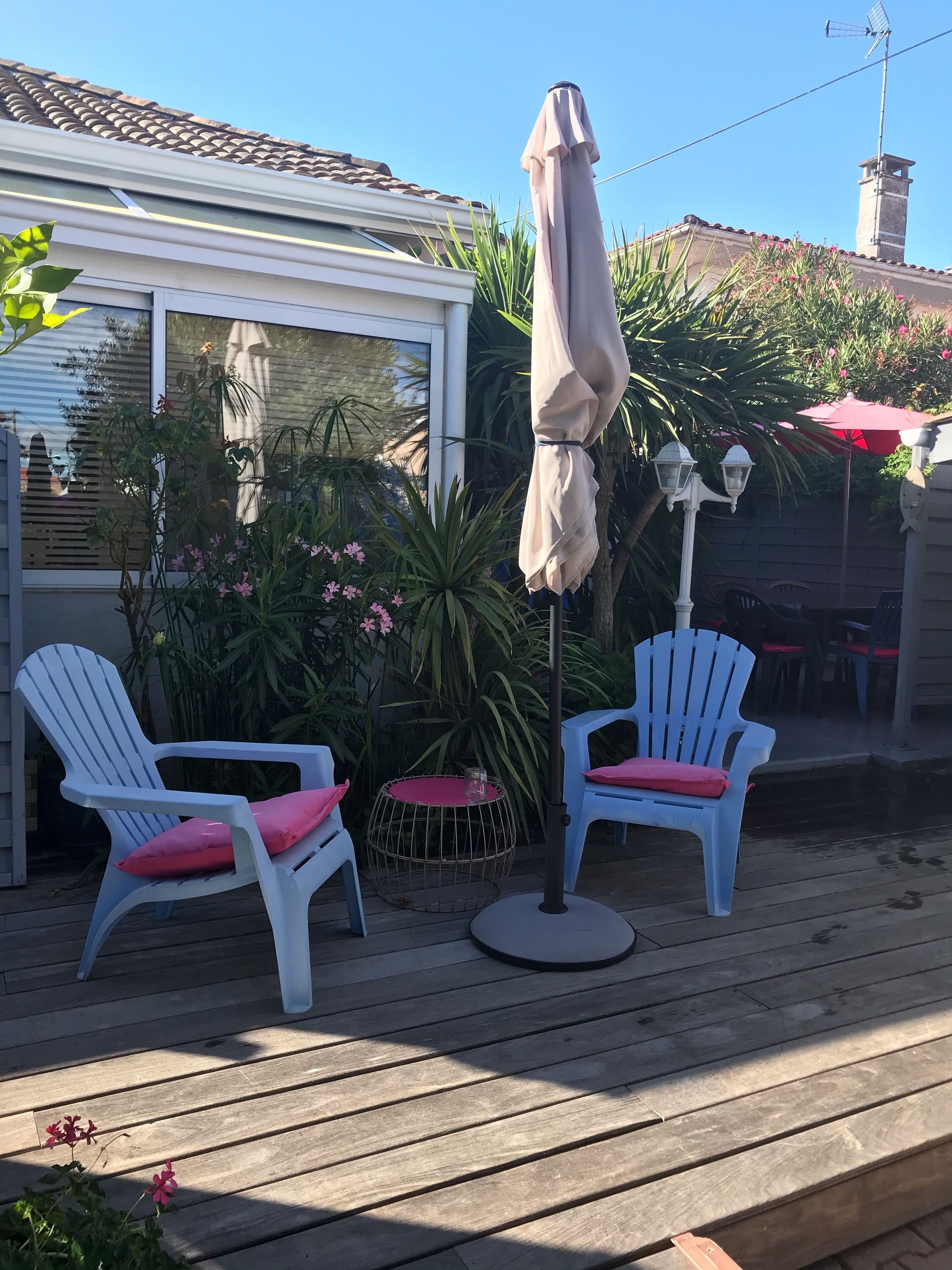 Una terraza con dos sillas Adirondack blancas y cojines rojos, una mesa redonda con una vela, y un gran paraguas.