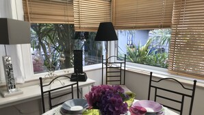 Une table à manger dressée avec des assiettes, des verres et un vase de fleurs, donnant sur un paysage verdoyant.