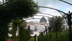 A covered pathway leading to a building with a dome, surrounded by greenery and metal arches. - House in Arcachon close to the beach, tastefully decorated, garden (Arcachon)