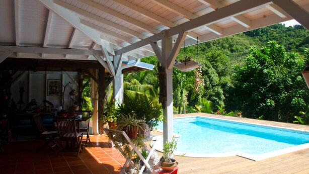 Un espace piscine extérieur doté d’un patio couvert, entouré d’une végétation luxuriante et avec une chaîne de montagnes en toile de fond.