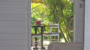 Une pièce avec un lit, une petite table sur laquelle est posé un vase de fleurs et une chaise. De la fenêtre, on peut admirer un paysage verdoyant.