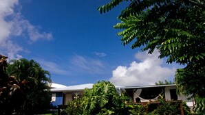 Une maison avec un toit blanc, entourée d’une végétation luxuriante et sous un ciel bleu dégagé.