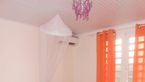 Une chambre à coucher comprenant un lit, une table de chevet, une lampe, une fenêtre avec des rideaux et un ventilateur de plafond.