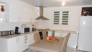 Une cuisine moderne avec des meubles blancs, une table à manger en bois et un panier de fruits.
