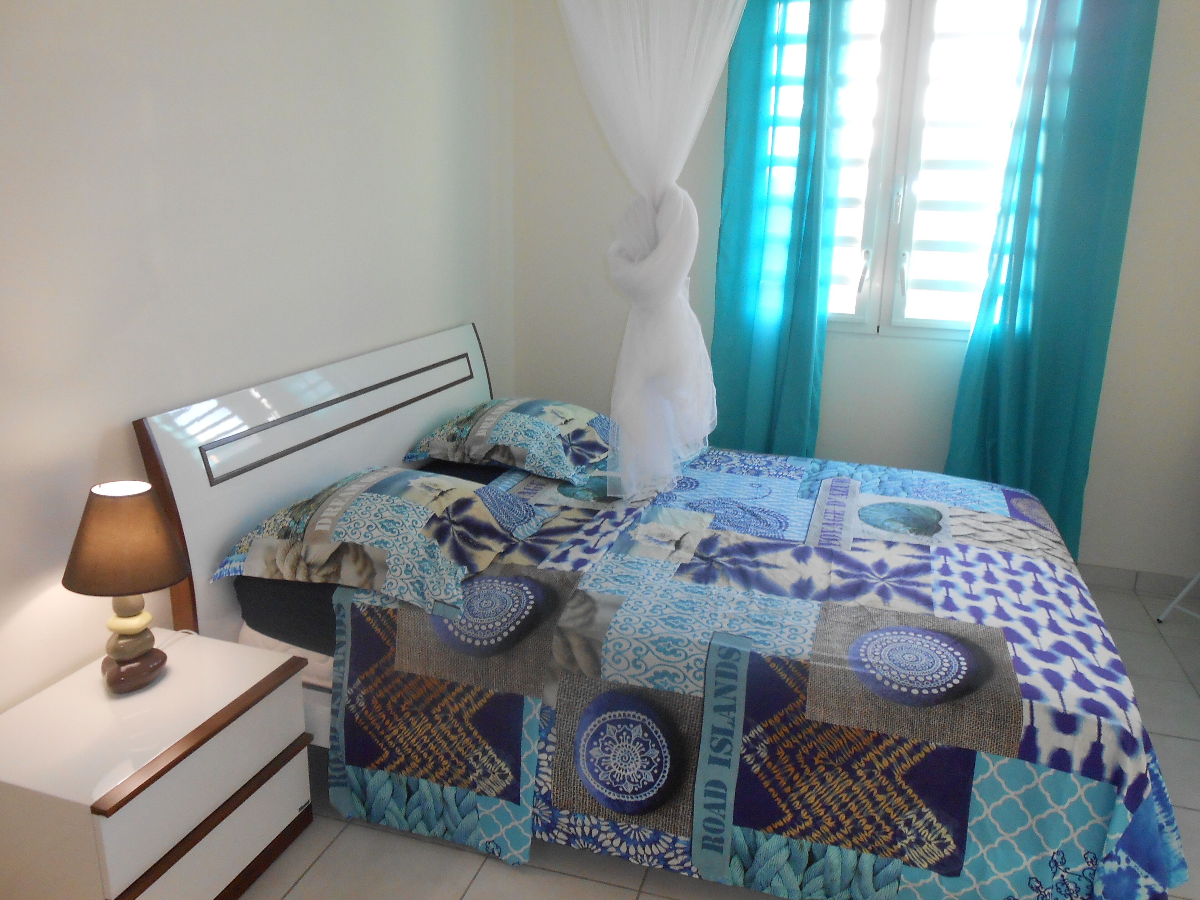 A bedroom with a bed covered in patterned bedding, a bedside table with a lamp, and a window with curtains.
