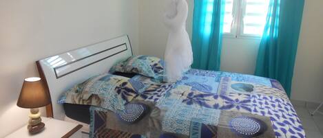 A bedroom with a bed covered in patterned bedding, a bedside table with a lamp, and a window with curtains.