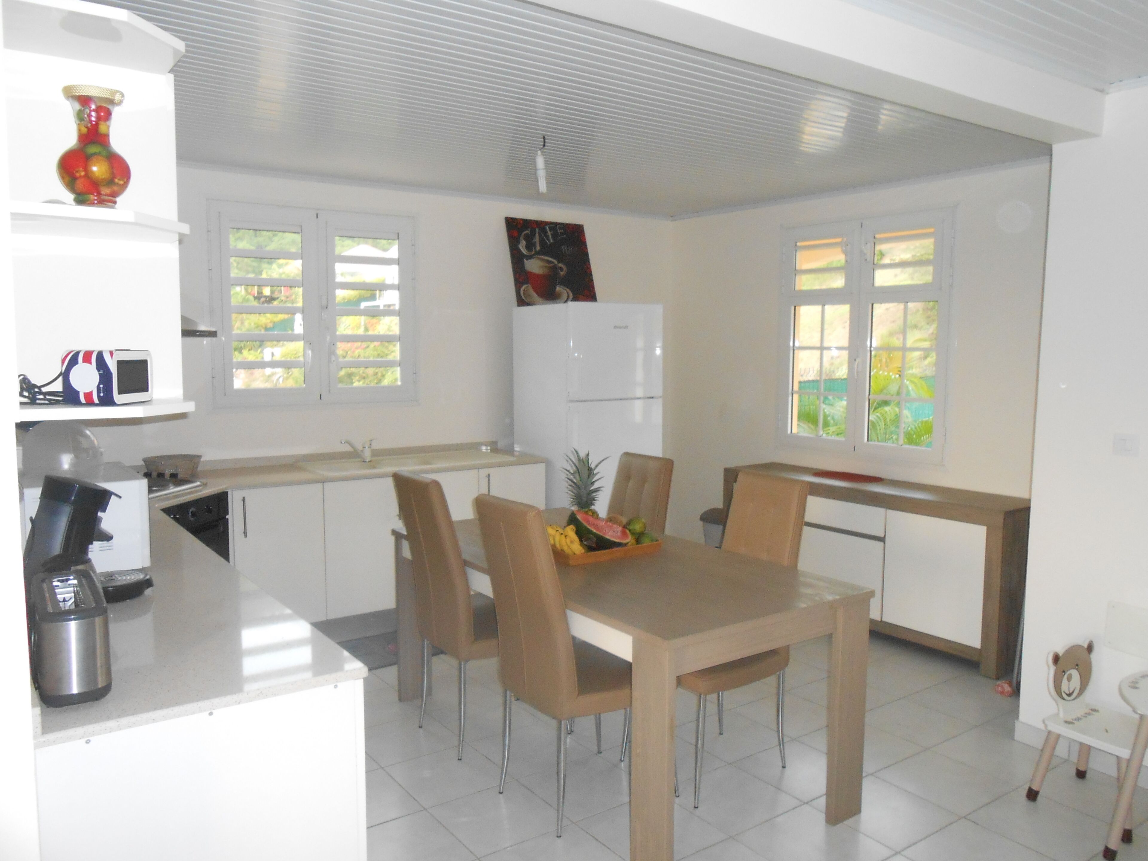 Une cuisine moderne avec des meubles blancs, une table à manger avec des chaises, un réfrigérateur et un four à micro-ondes.