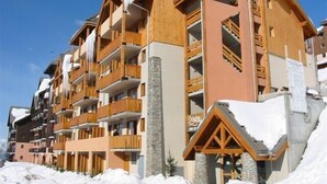 Un hôtel à plusieurs étages, doté de balcons en bois et de piliers en pierre, entouré de neige.