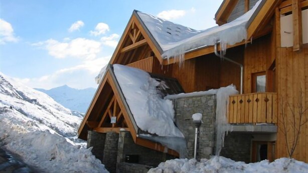 Un chalet en bois, avec des fondations en pierre, un balcon et un toit partiellement effondré, recouvert de neige.