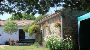 Un edificio de piedra con tejado de tejas, un banco y un jardín con flores y arbustos.