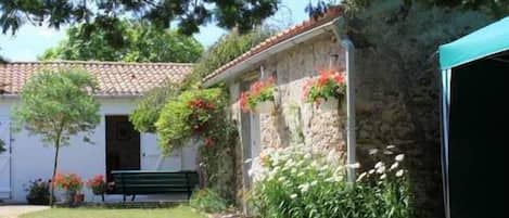 Un edificio de piedra con tejado de tejas, un banco y un jardín con flores y arbustos.