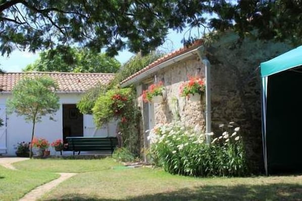 Un edificio de piedra con tejado de tejas, un banco y un jardín con flores y arbustos.