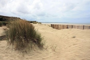 Una playa arenosa con una cerca de madera y dunas cubiertas de hierba.