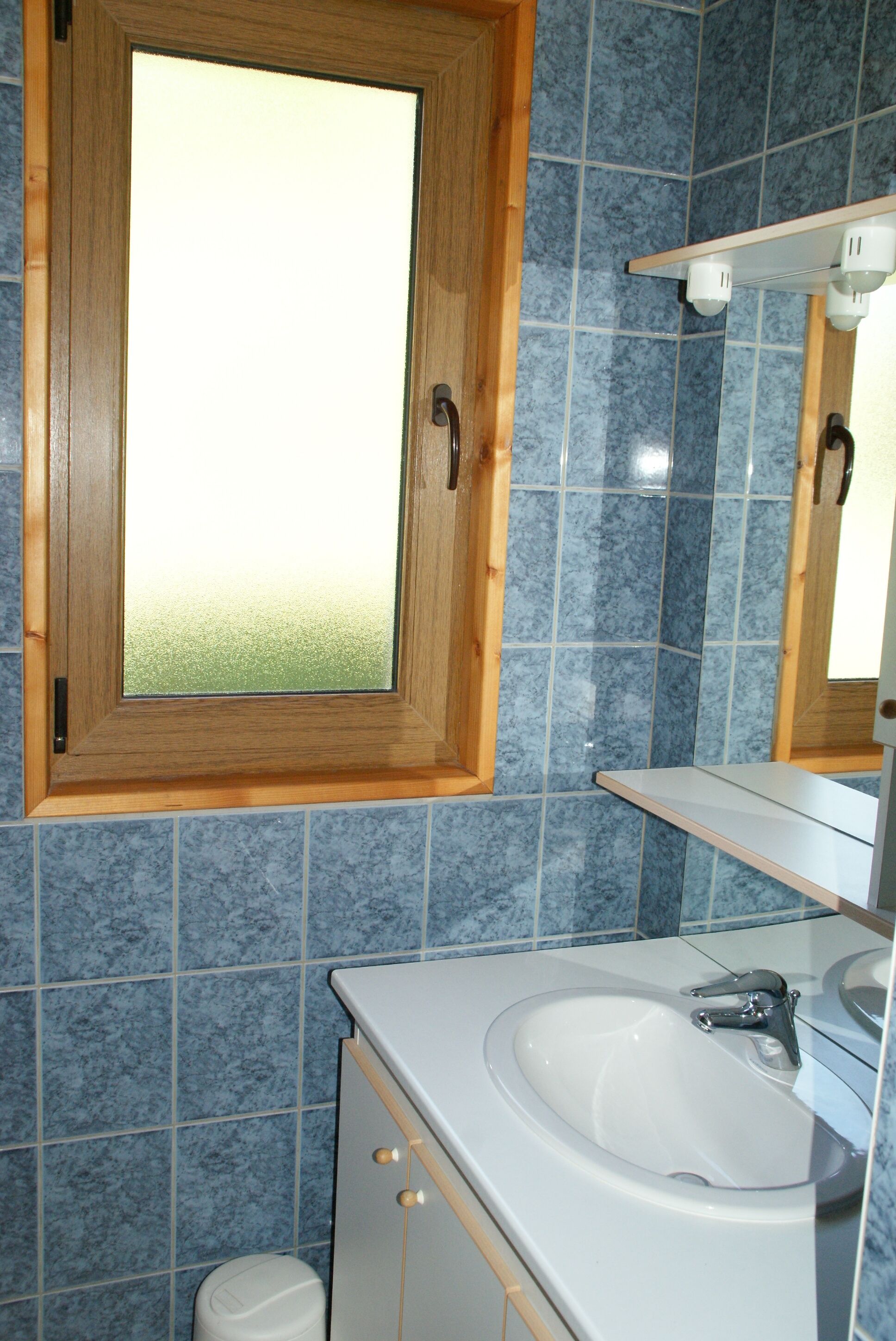 A bathroom with a wooden medicine cabinet, a white sink, and blue-tiled walls.