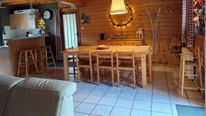 A cozy cabin interior with a wooden dining table, bar stools, a sofa, and a kitchen area. - Chalet des Etangs in La Bresse for 8 people (La Bresse)