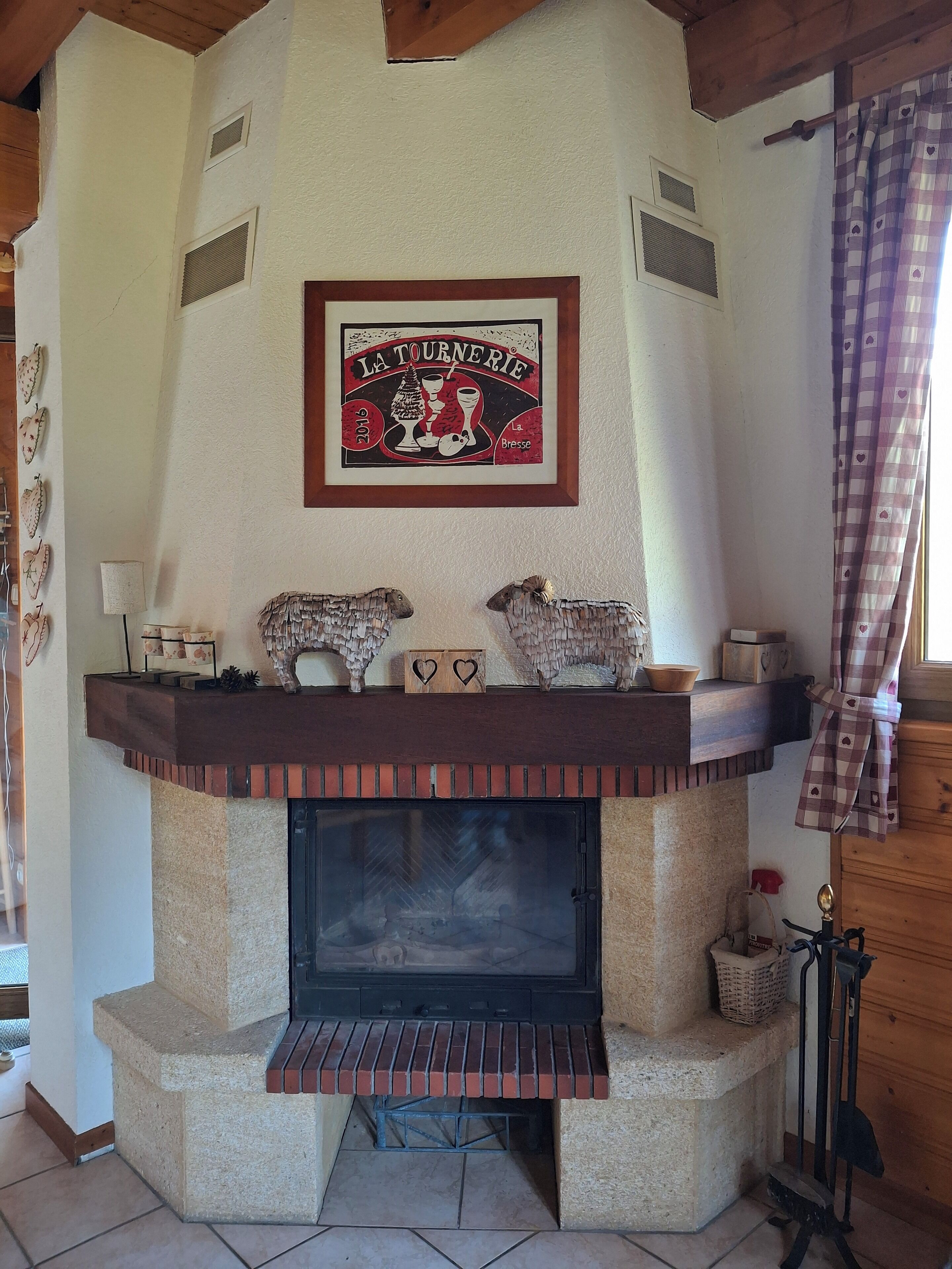 Une cheminée surmontée d’un cadre décoratif, une étagère avec des objets décoratifs et une fenêtre avec des rideaux.