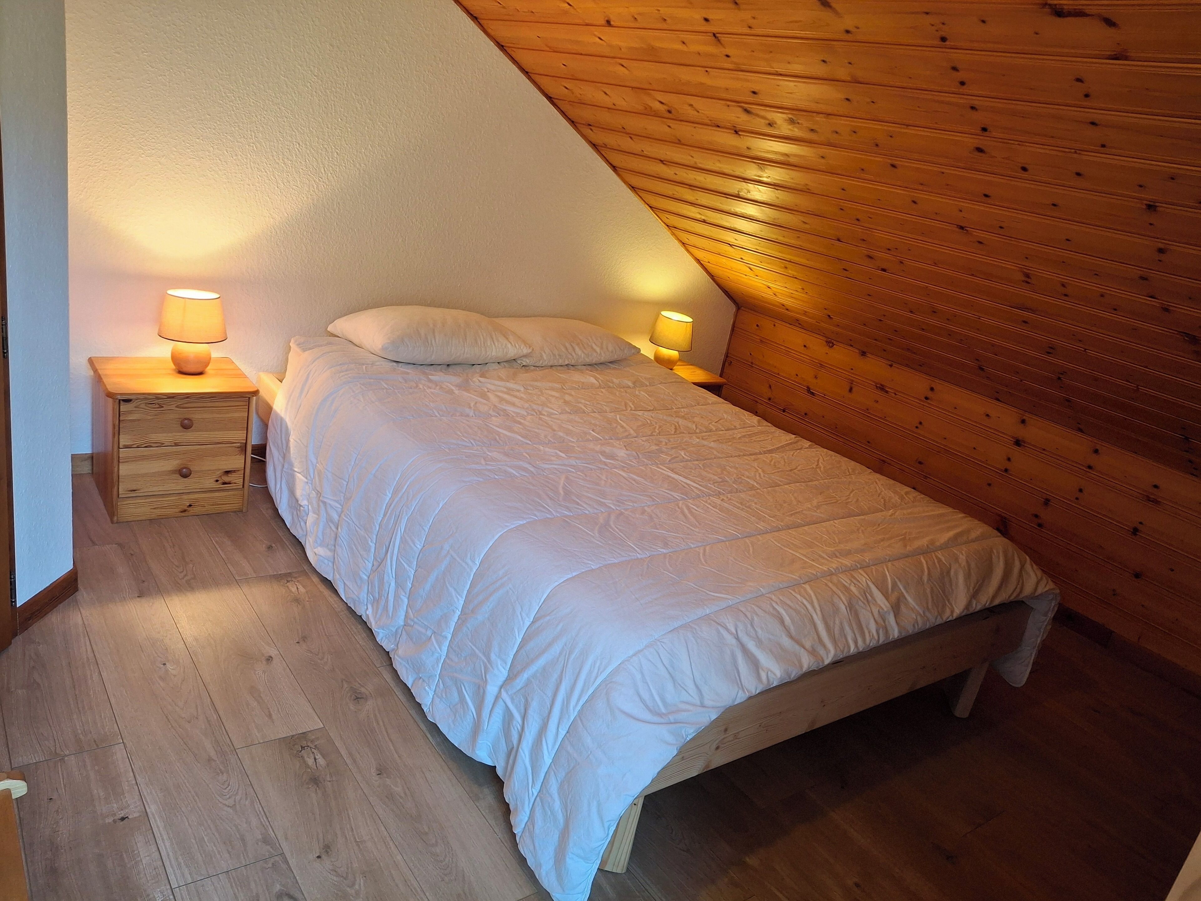 Ein Schlafzimmer mit Holzbalkendecke, einem Einzelbett mit weißer Bettwäsche, zwei Nachttischlampen und einem Nachttisch mit Schubladen.