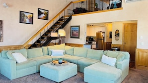 A living room with a sectional sofa, a coffee table, a staircase, and a kitchen area.