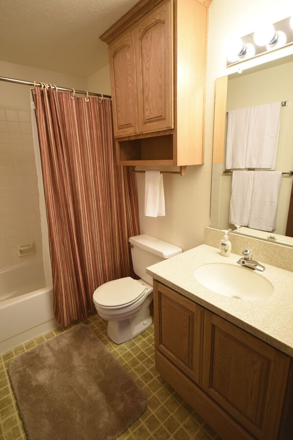A bathroom with a shower curtain, toilet, sink, and wooden cabinets.