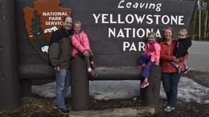 Een gezin van vier zit op een bankje voor een bord met daarop Yellowstone National Park.