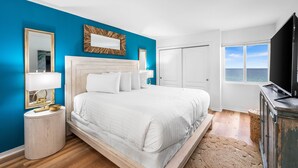 Une chambre à coucher avec un lit, une table de chevet, un miroir, une télévision et une vue sur l’océan.